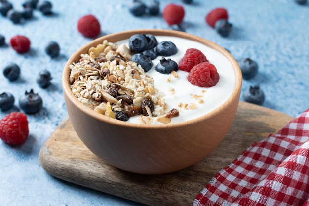 Yogur con bayas y muesli para el desayuno en un tazón sobre fondo azul.