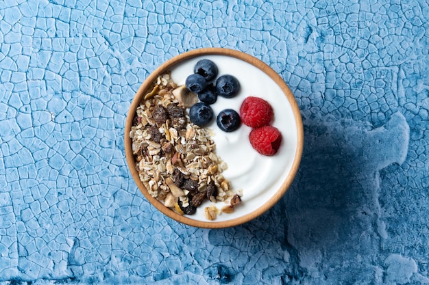 Yogur con bayas y muesli para el desayuno en un tazón sobre fondo de lbue