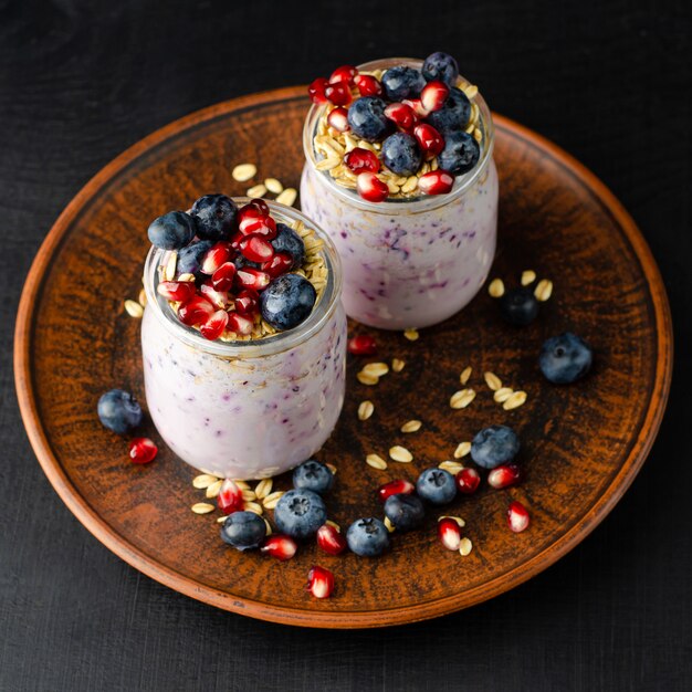 Yogur casero con arándanos, semillas de granada y avena en la oscuridad. Vista superior, imagen cuadrada