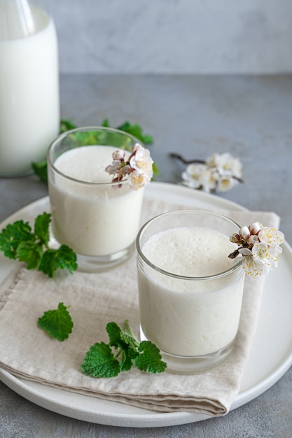 Yogur casero fresco en dos vasos con hierbas y flores sobre una pared gris. Probiótico de bebida láctea fermentada fría.