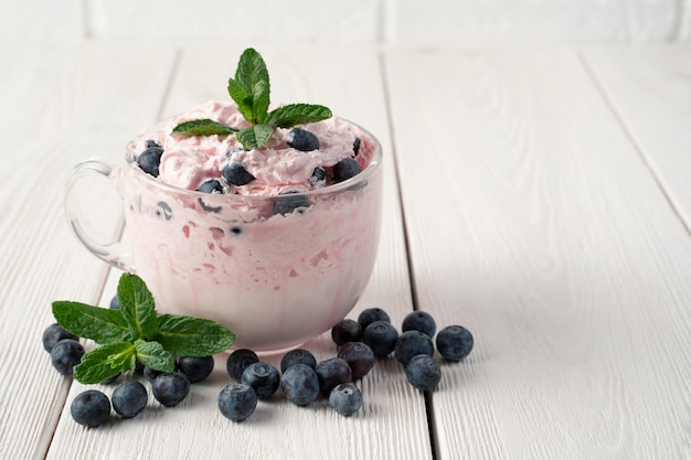 Yogur con crema y bayas en una mesa blanca.