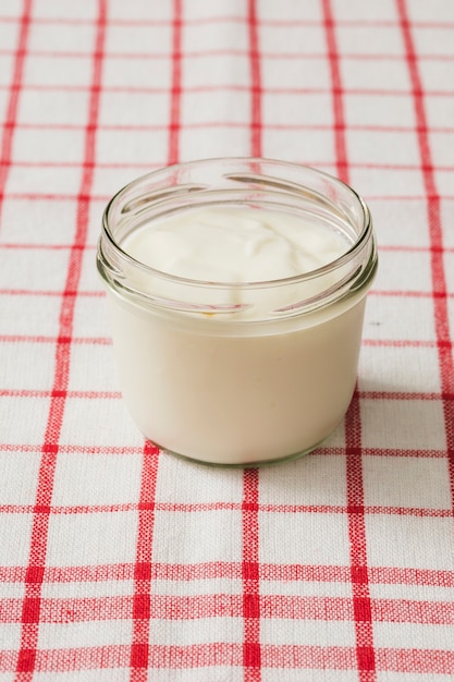 Yogur cremoso fresco en el tarro de cristal en la servilleta a cuadros