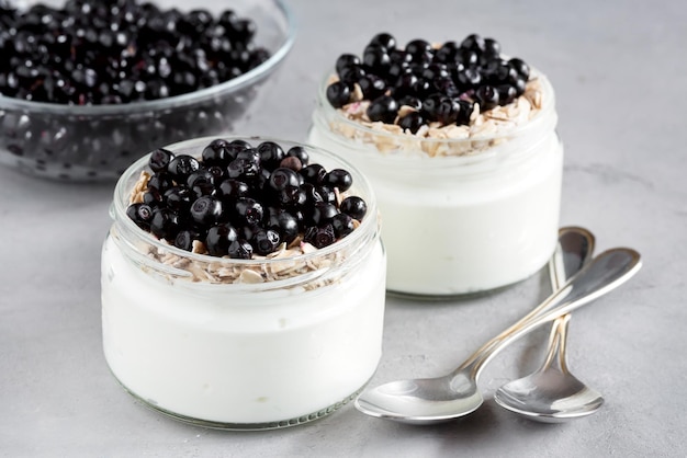 Yogur de desayuno saludable con arándanos y muesli servido en frasco de vidrio sobre fondo de madera de color