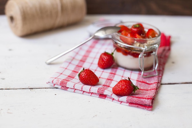 Foto yogur dulce con deliciosas fresas frescas y copos de avena. carrete de hilo en el fondo