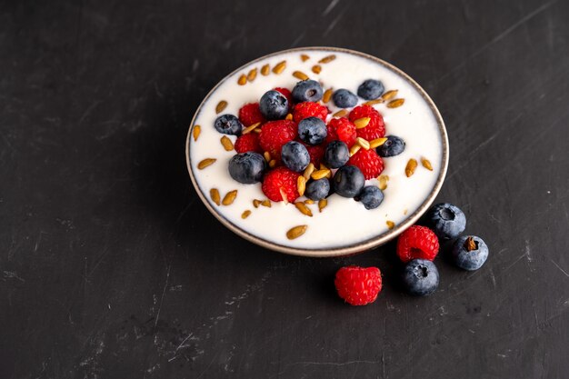 Yogur de frambuesas de arándano fresco sabroso batido de postre en tazón de cerámica de pie sobre la mesa negra. Batido casero de bayas. Alimentación saludable. Comida dietetica. yogur