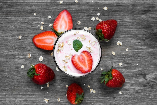 Yogur de fresa en un vaso con bayas frescas, avena y menta sobre fondo de madera rústica