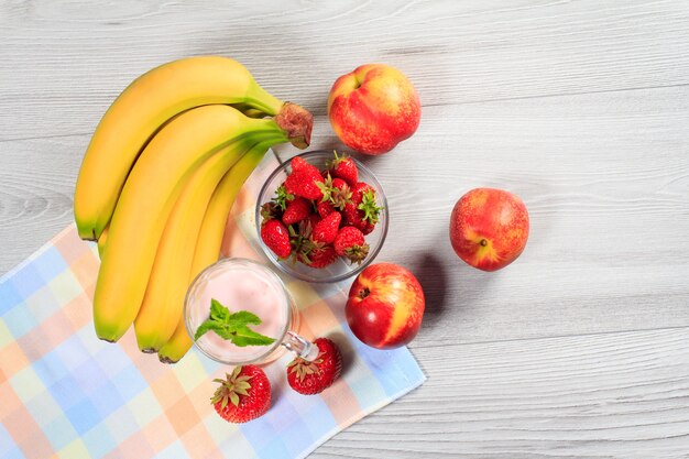 Yogur de fresa en un vaso con fresas frescas, nectarina, plátano en una mesa de madera con una servilleta Vista superior