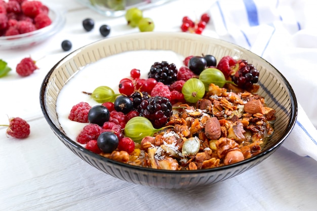 Yogur, granola y bayas frescas en un recipiente sobre una mesa de madera