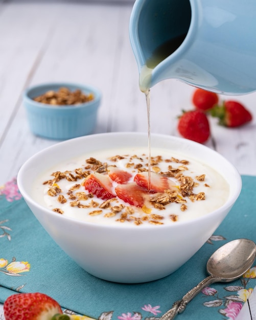 Yogur con granola de fresa y miel en un bol sobre una mesa de madera blanca