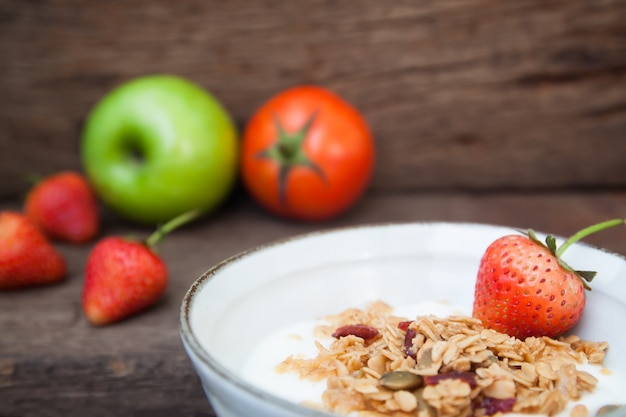 Yogur griego con granola y fresa en un recipiente con manzana verde y tomate