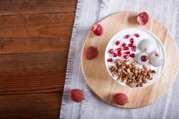 Yogur griego con lichi, semillas de granada y granola en un plato blanco sobre un fondo de madera marrón