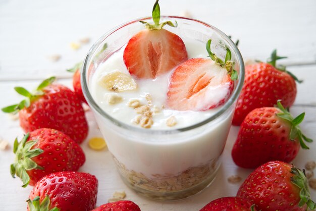 Yogur griego sano con las fresas y el muesli en el vidrio en un de madera viejo.