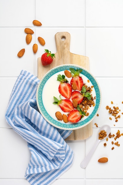 Yogur griego en un tazón blanco con ingredientes para hacer desayuno granola y fresas frescas