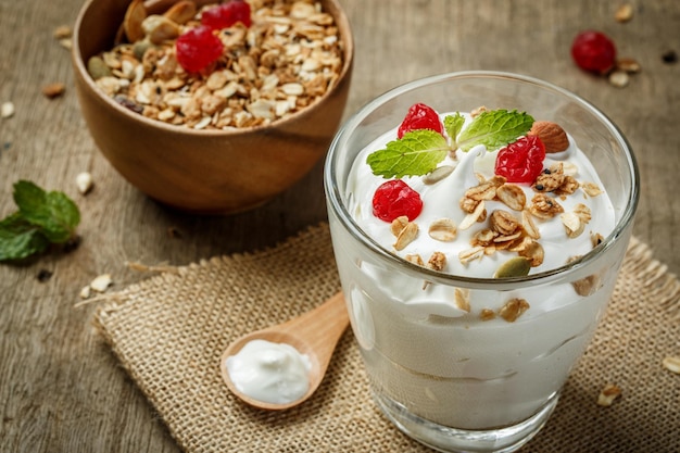 Yogur griego en un vaso con cucharas sobre un fondo de madera