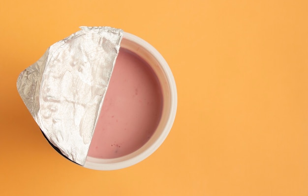 Foto yogur rosa con arándanos en un vaso de plástico abierto sobre una superficie de papel melocotón. vista superior, espacio para texto.