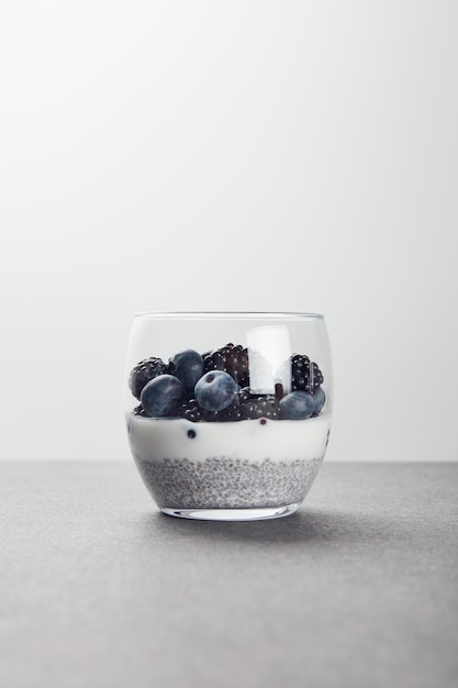 Foto yogur sabroso con semillas de chía arándanos y moras en superficie de mármol aislados en gris