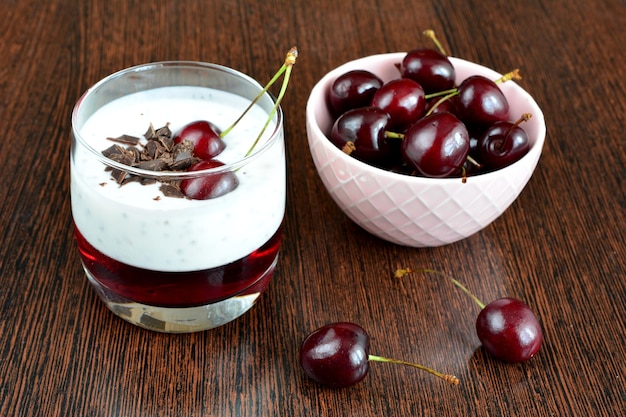 yogur con semillas de chía, chocolate y jalea de cereza en vaso de beber en una tabla de madera oscura