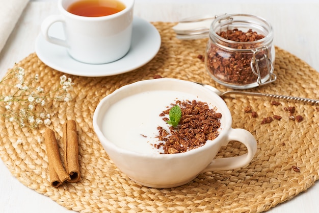 Yogurt con chocolate granola en taza, desayuno con té en beige