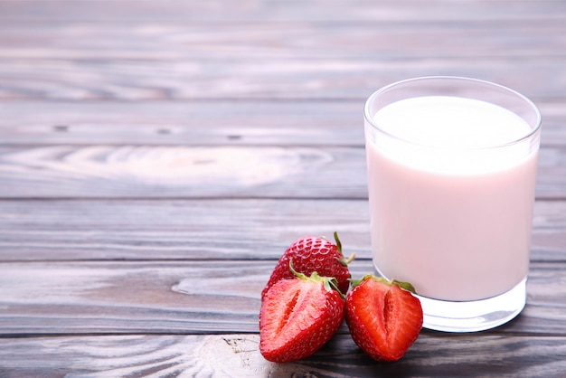 Yogurt con fresa en vaso sobre madera marrón.