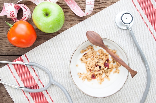 Yogurt con granola en un tazón y un estetoscopio en la mesa de madera