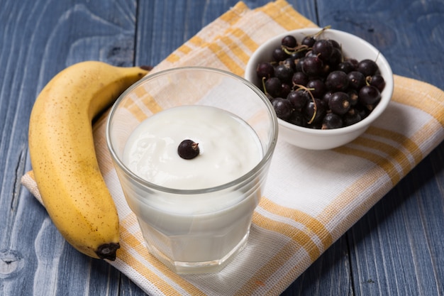 Yogurt en un vaso, plátano y grosella sobre tablas de madera