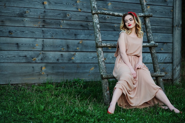 Yong menina loira elegante no vestido rosa na escadaria de madeira de fundo de jardim.