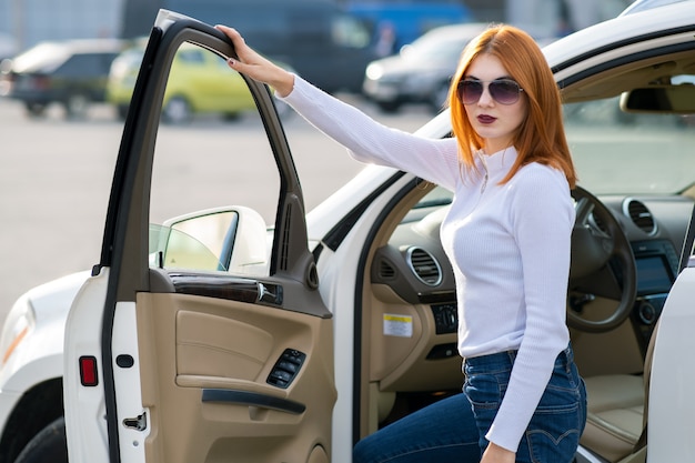 Yong mulher bonita em pé perto de um grande carro todo terreno ao ar livre. Garota de motorista em roupas casuais fora de seu veículo.