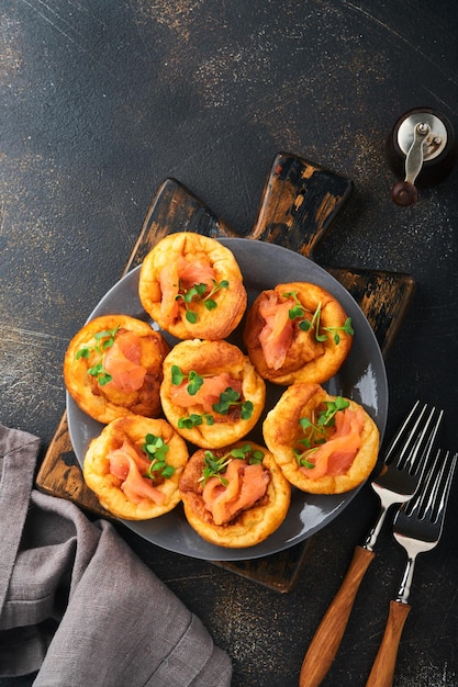 Yorkshire-Pudding Traditioneller englischer Yorkshire-Pudding mit Lachs- und Rettich-Microgreens-Beilage auf dunkelgrauer Platte und dunkler Hintergrundtabelle Draufsicht