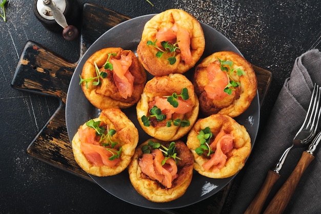 Yorkshire-Pudding Traditioneller englischer Yorkshire-Pudding mit Lachs- und Rettich-Microgreens-Beilage auf dunkelgrauer Platte und dunkler Hintergrundtabelle Draufsicht