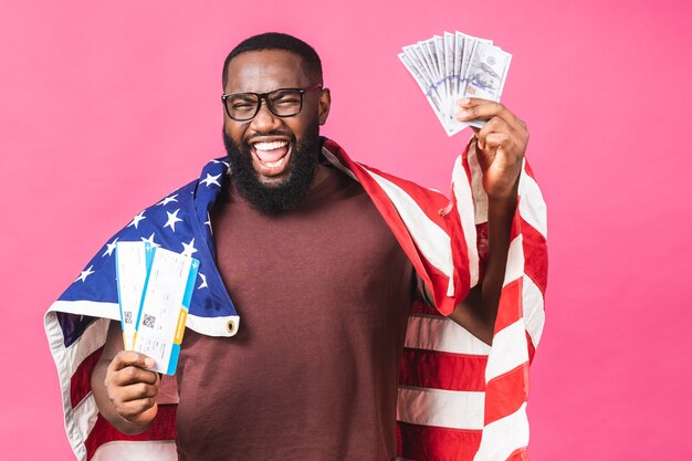 Young African American Black Man Holding Boarding Pass Tickets und Dollar-Geldscheine isoliert über rosa Hintergrund.