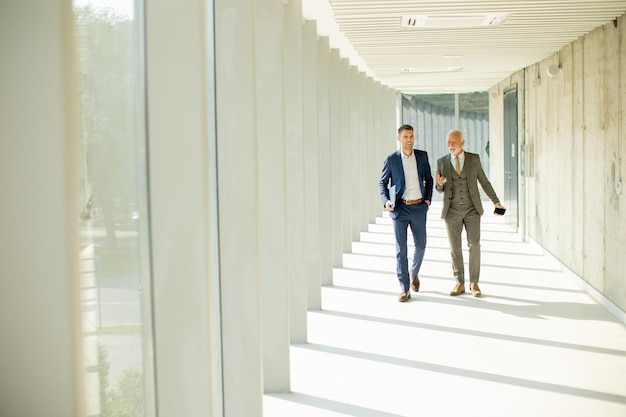 Young e um empresário sênior caminham pelo corredor de um escritório em uma conversa profunda