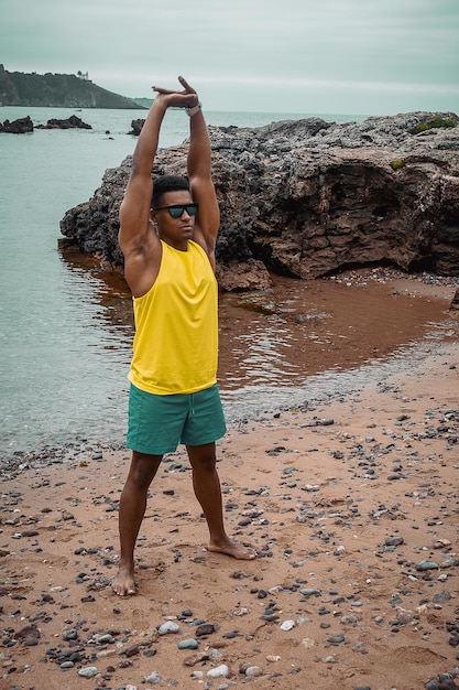 Young fit hombre con gafas de sol trabajando con el océano y las rocas en un fondo