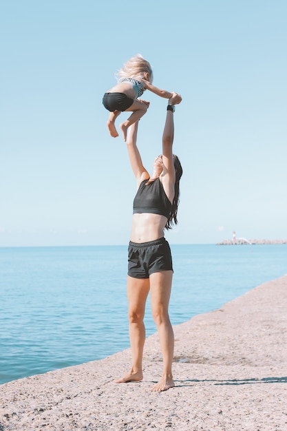 Young fit mujer mamá con linda niña haciendo ejercicio en la playa juntos