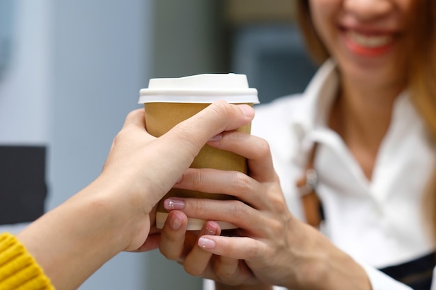 Young woman barista serving take away coffee paper cup with smiling face in cafe