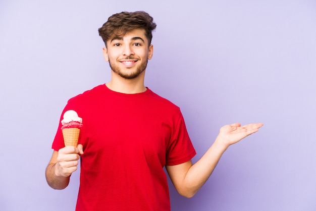 Youngian homem segurando um sorvete mostrando um espaço de cópia na palma da mão e segurando a outra mão na cintura