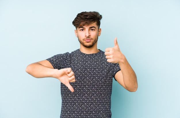 Youngian Mann isoliert auf einer blauen Wand, die Daumen hoch und Daumen runter zeigt