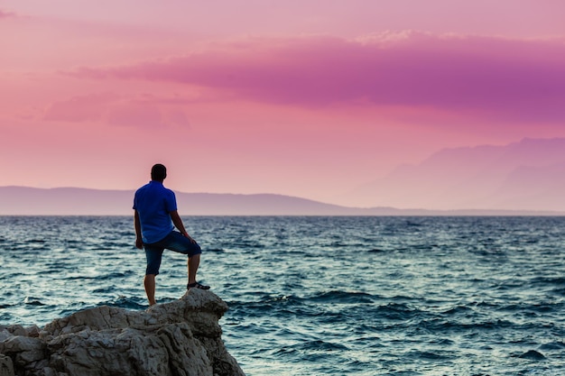 Yung-Mann, der auf einem Felsen steht und den Sonnenuntergang auf dem Meer betrachtet