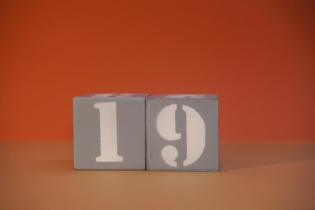 Zahl 19 auf grauen Holzwürfeln in Großaufnahme Konzept der Datums- und Uhrzeitangabe Mathe-Konzept Kopierraum für Text oder Ereignis Weiße Zahlen 19 auf Bausteinen mit orangefarbenem Hintergrund Lernwürfel Selektiver Fokus