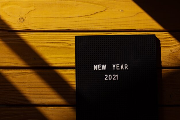 Zahlen 2021 auf Briefbrett auf gelbem Holzhintergrund mit Sonnenlicht. Neues Konzept für das Jahr 2021, Ansicht von oben.