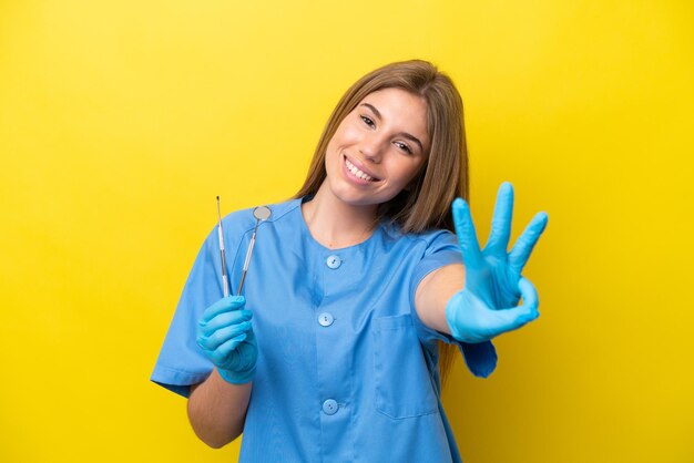 Zahnärztin, kaukasische Frau, die Werkzeuge isoliert auf gelbem Hintergrund hält, glücklich und drei mit den Fingern zählend