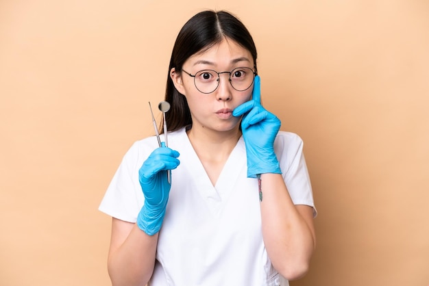 Zahnarzt Chinesin hält Werkzeuge isoliert auf beigem Hintergrund und denkt an eine Idee