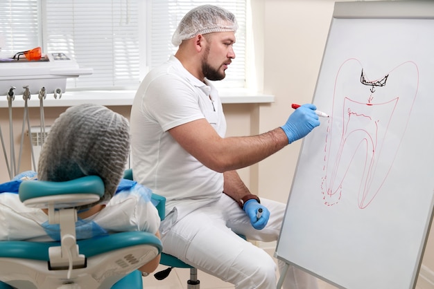 Zahnarzt, der Bild des Zahns auf weißer Tafel in der Zahnarztpraxis zeichnet