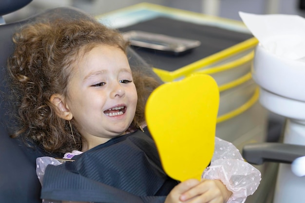 Zahnarzt Kind. Untersuchung Behandlung Zähne Kinder. medizinische Untersuchung der Mundhöhle. Glückliches Kindermädchen, das geheilte Zähne im Spiegel betrachtet.