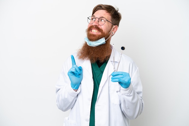 Zahnarzt rötlicher Mann mit Werkzeugen isoliert auf weißem Hintergrund, der auf eine großartige Idee zeigt