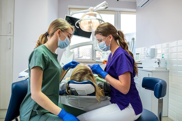 Zahnarzt und Assistentin in Masken und Uniformen, die eine professionelle Zahnreinigungspatientin machen