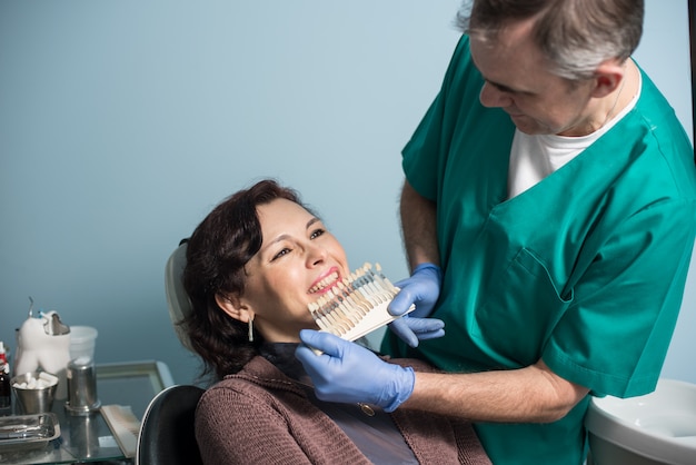 Zahnarzt und weiblicher Patient, die Farbe der Zähne im zahnmedizinischen Klinikbüro überprüfen und vorwählen