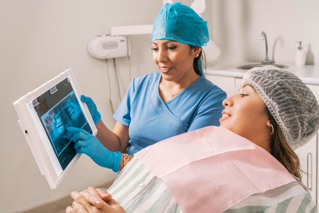 Zahnarzt zeigt einem Patienten, der auf einer Trage in einer Zahnklinik liegt, ein Röntgenbild