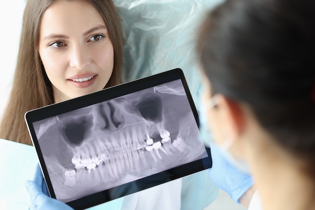 Zahnarztarzt, der digitales Tablet mit Zahnröntgen vor dem Patienten hält