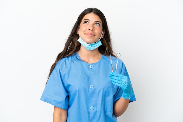 Zahnarztfrau, die Werkzeuge über isoliertem weißem Hintergrund hält und nach oben schaut