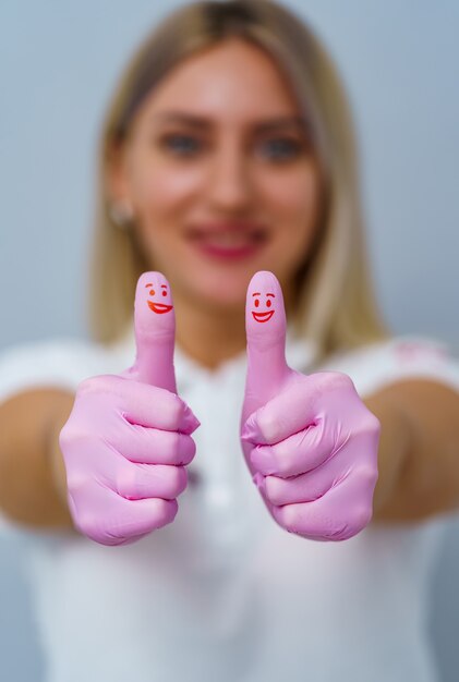 Zahnarztfrau mit rosa Handschuhen. Cooles Zeichen anzeigen. Rotes Lächeln auf den Daumen.